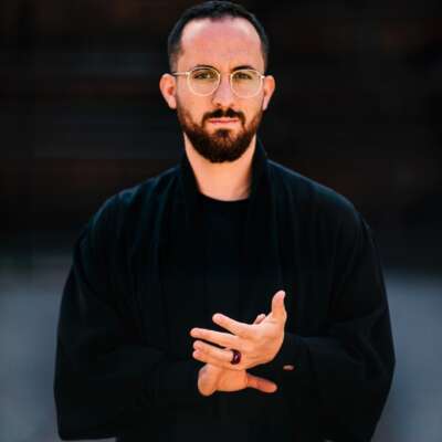 Igor Levit mit gefalteten Händen und Brille vor einem schwarzen Hintergrund