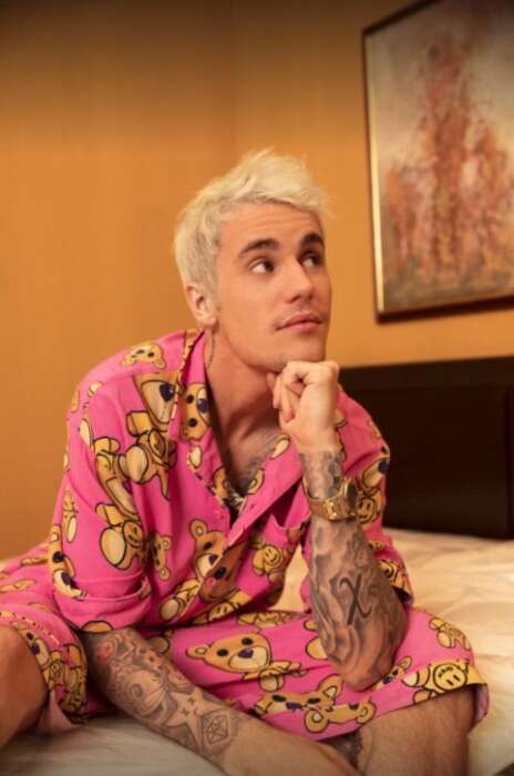 Justin Bieber sitzt in einem rosanen Schlafanzug auf einem Bett und stützt seinen Kopf auf seiner Hand ab.
