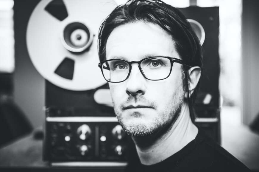 Steven Wilson steht in einem schwarz/weiß-Foto vor einem Tonbandgerät.