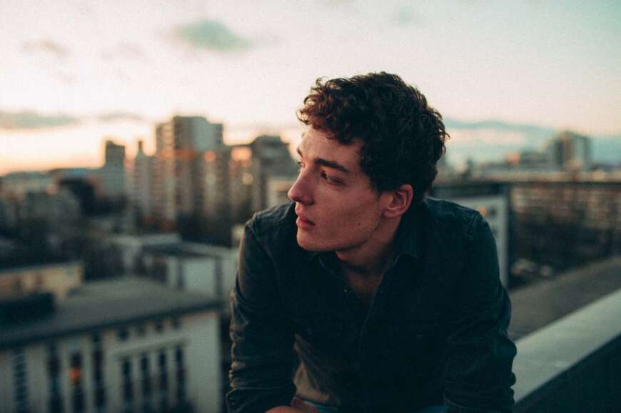 Till Seifert sitzt in einem schwarzen Pullover im Vordergrund des Bildes. Im Hintergrund sind Hochhäuser zu sehen.