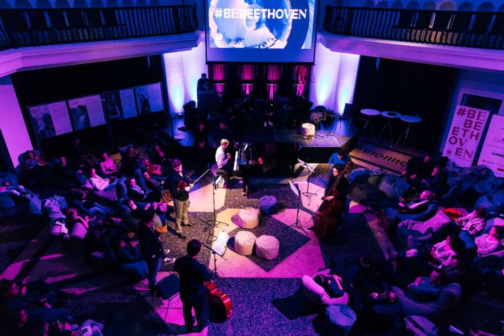 Eine Gruppe von Musiker*innen steht in einem violett ausgeleuchteten Raum und spielt für ein Publikum, das am Rand sitzt. Konzert im Rahmen von BeBeethoven, eine Themenwoche zum 250. Geburtstag von Ludwig van Beethoven.