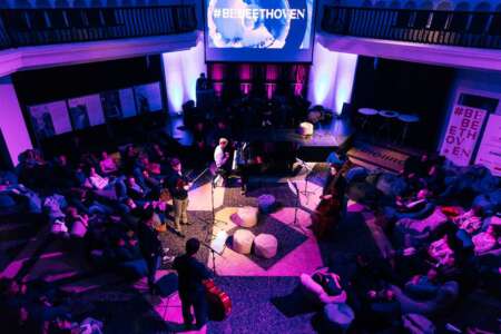 Eine Gruppe von Musiker*innen steht in einem violett ausgeleuchteten Raum und spielt für ein Publikum, das am Rand sitzt. Konzert im Rahmen von BeBeethoven, eine Themenwoche zum 250. Geburtstag von Ludwig van Beethoven.