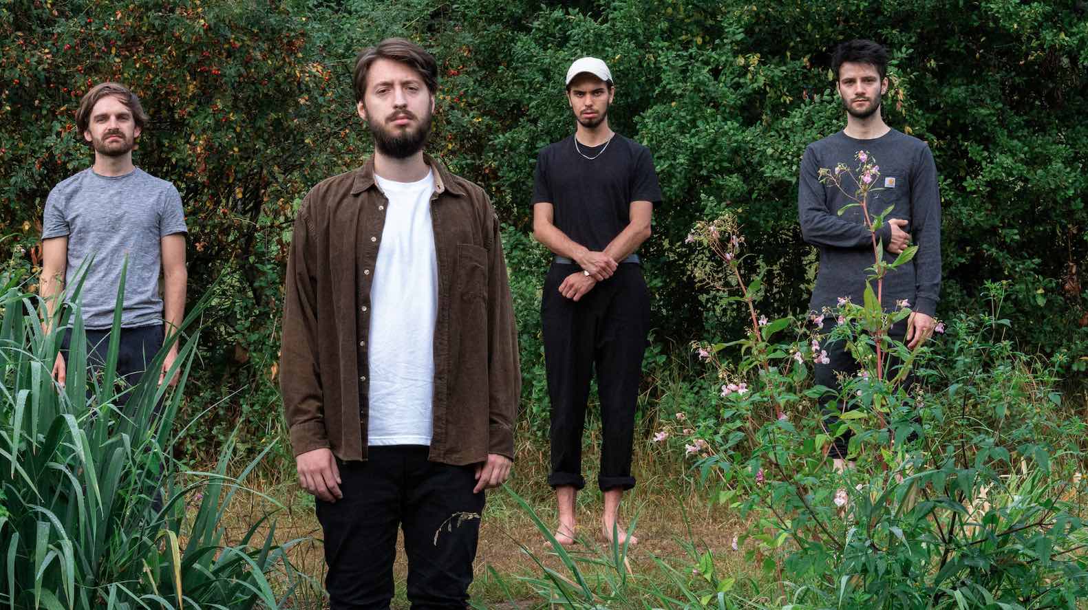 Die vier Bandmitglieder von Fil der Protagoniost stehen draußen vor einer grünen Hecke