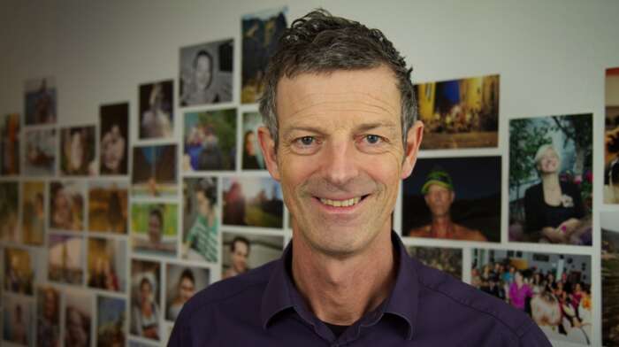Daniel Sponsel, der Leiter des DOK.fest München, steht vor einer Wand mit Fotografien. Er ist von der Brust aufwärts fotografiert. In seinem Essay spricht er über das Verhältnis von Kino und digitalen Formaten.
