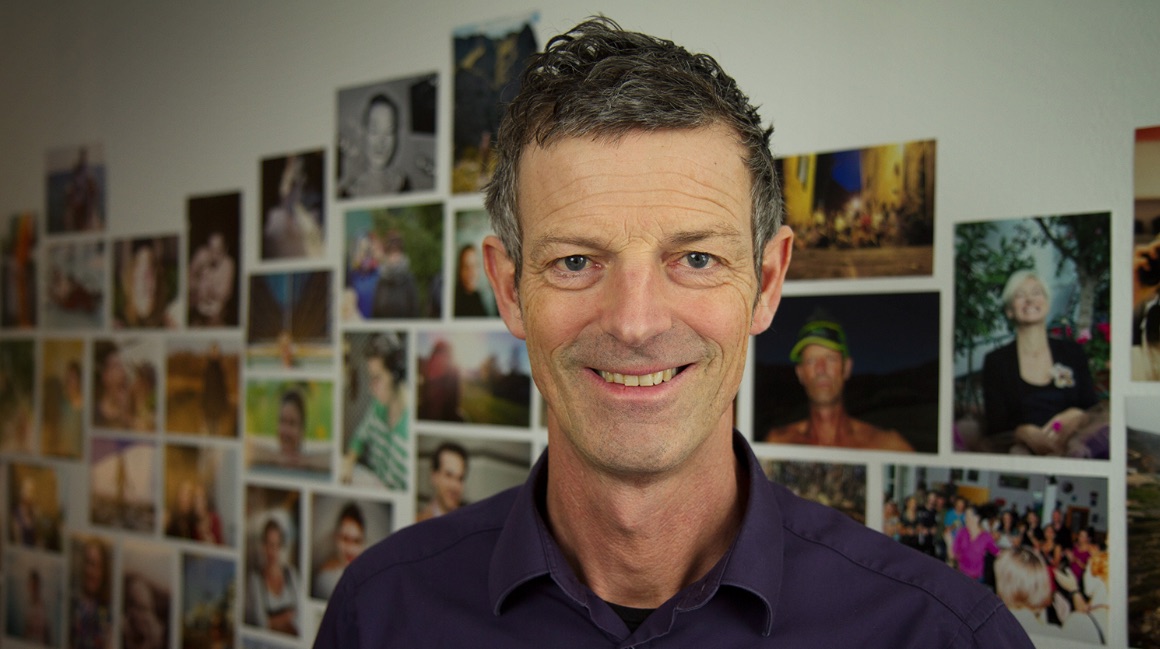 Daniel Sponsel, der Leiter des DOK.fest München, steht vor einer Wand mit Fotografien. Er ist von der Brust aufwärts fotografiert. In seinem Essay spricht er über das Verhältnis von Kino und digitalen Formaten.