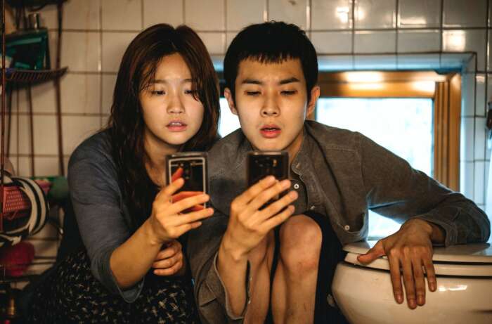 Szenenbild aus Parasite: Ki Jung (Park So-dam) und Ki Woo (Choi Woo-shik) knien mit dem Smartphone in der Hand neben der Toilette.