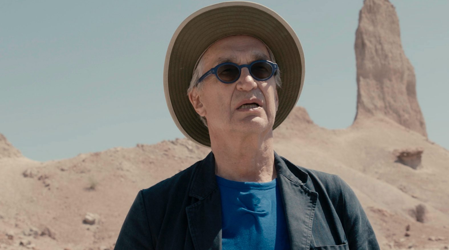 Wim Wenders während der Dreharbeiten zu "Desperado": Ein Mann mit Hut und blauer Sonnenbrille vor karger Landschaft