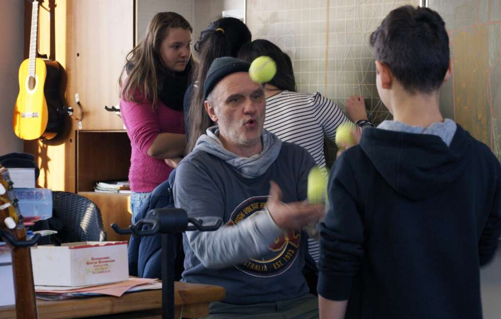 Herr Bachmann jongliert im Klassenzimmer, umgeben von seiner Klasse.