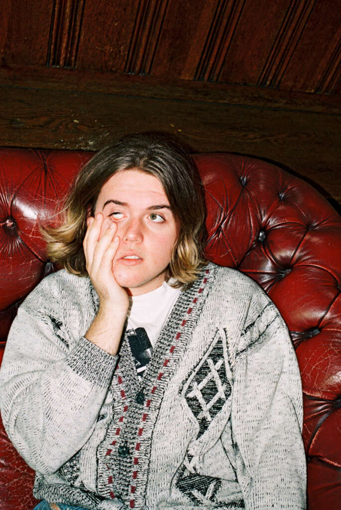 Mann Rote Couch Grauer Sweater Müder Gesichtsausdruck