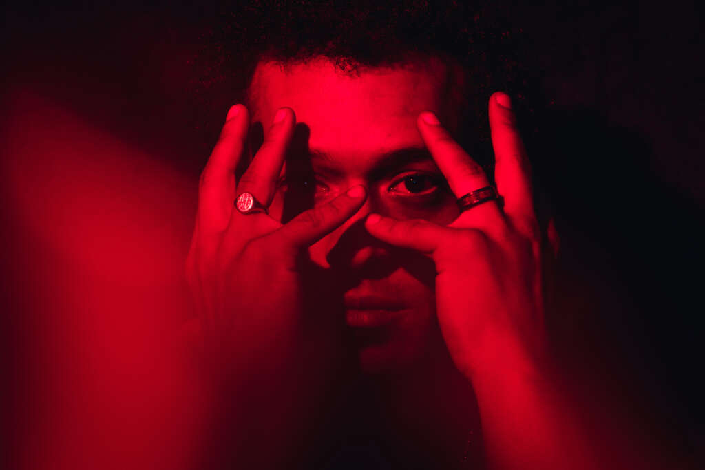 Makaya McCraven schaut durch seine beringten Finger in rotem Licht.