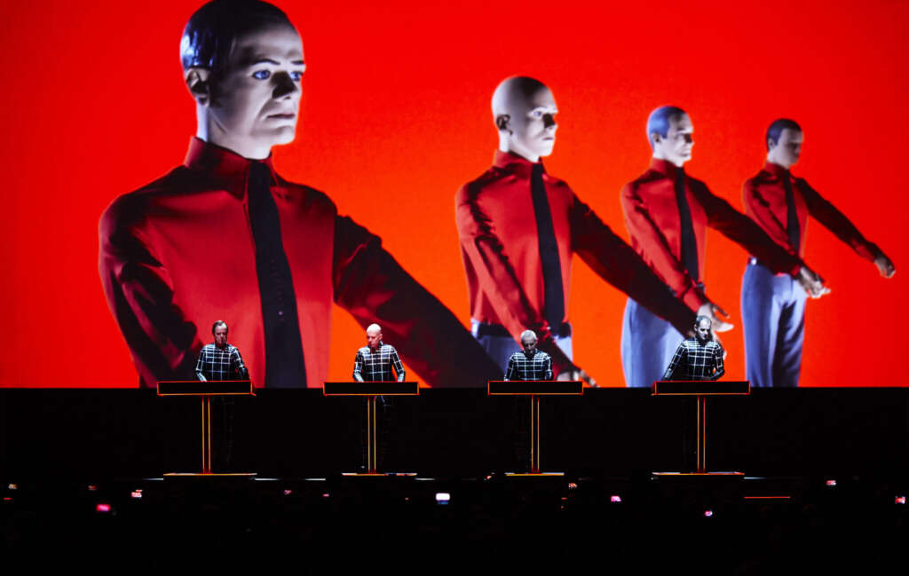 Ein Bild der Gruppe Kraftwerk während einer Performance an Synthesizern vor rotem Hintergrund, aus der Kunstsammlung NRW Düsseldorf 2013.