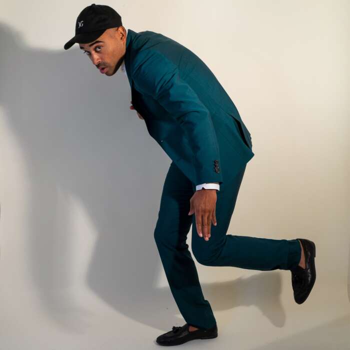 Sänger Patrice tanzt mit schwarzer Cap und in einem petrolfarbenen Anzug vor weißem Hintergrund.