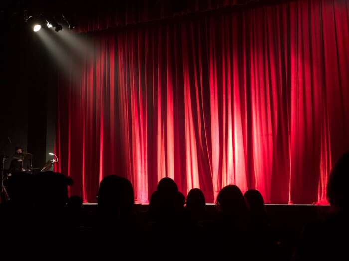 Eine roter Bühnenvorhang, Publikum und ein Spotlight, dass verrät: gleich geht die Show los.
