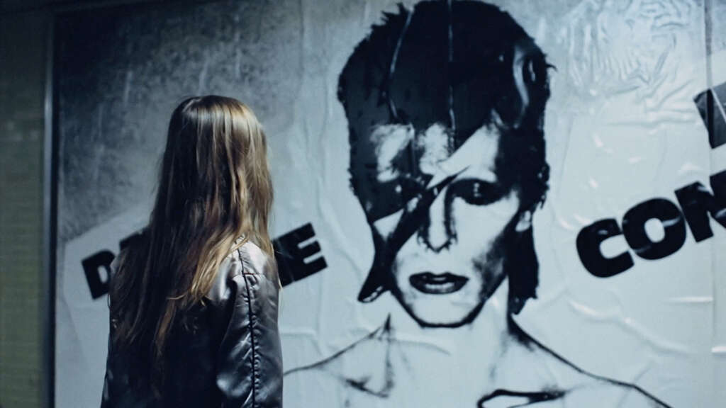 Eine Filmsequenz aus „CHRISTIANE F. – Wir Kinder vom Bahnhof Zoo“ ist zu sehen: Christiane schaut ein Konzertplakat von David Bowie an.