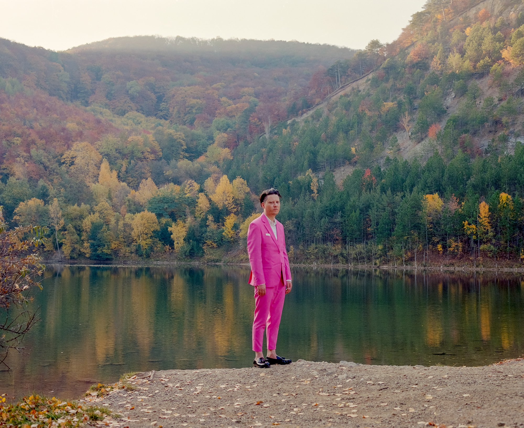 Portraitfoto Konstantin Gropper alias Get Well Soon in einem pinken Anzug am Ufer eines Sees in der Natur