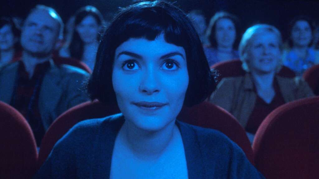 Zu sehen ist die junge, dunkelhaarige Amélie Poulain im Kino, so blickt mit großen Augen in die Kamera.