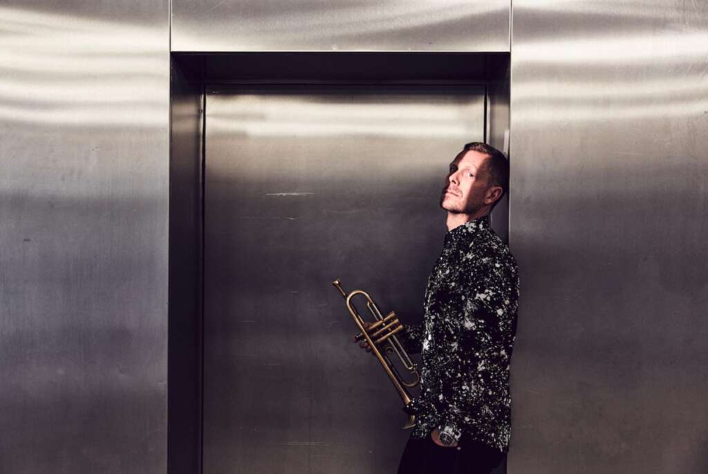 Portraitfoto Nils Wülker mit Trompete vorm Fahrstuhl