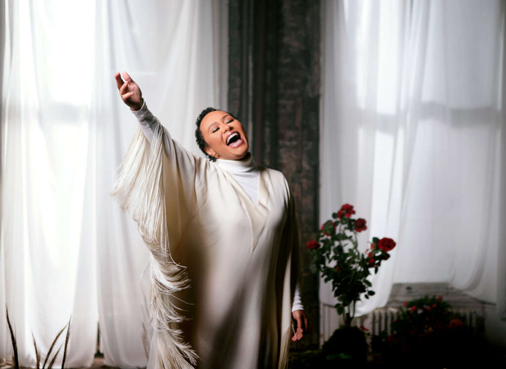 Portraitfoto Emeli Sandé im weißen Kleid, Rosen im Hintergrund