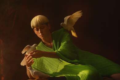 Portraitfoto Kat Frankie, im grünen Kleid, zur Seite geneigt mit weißer Tauben in der Hand und auf der Schulter