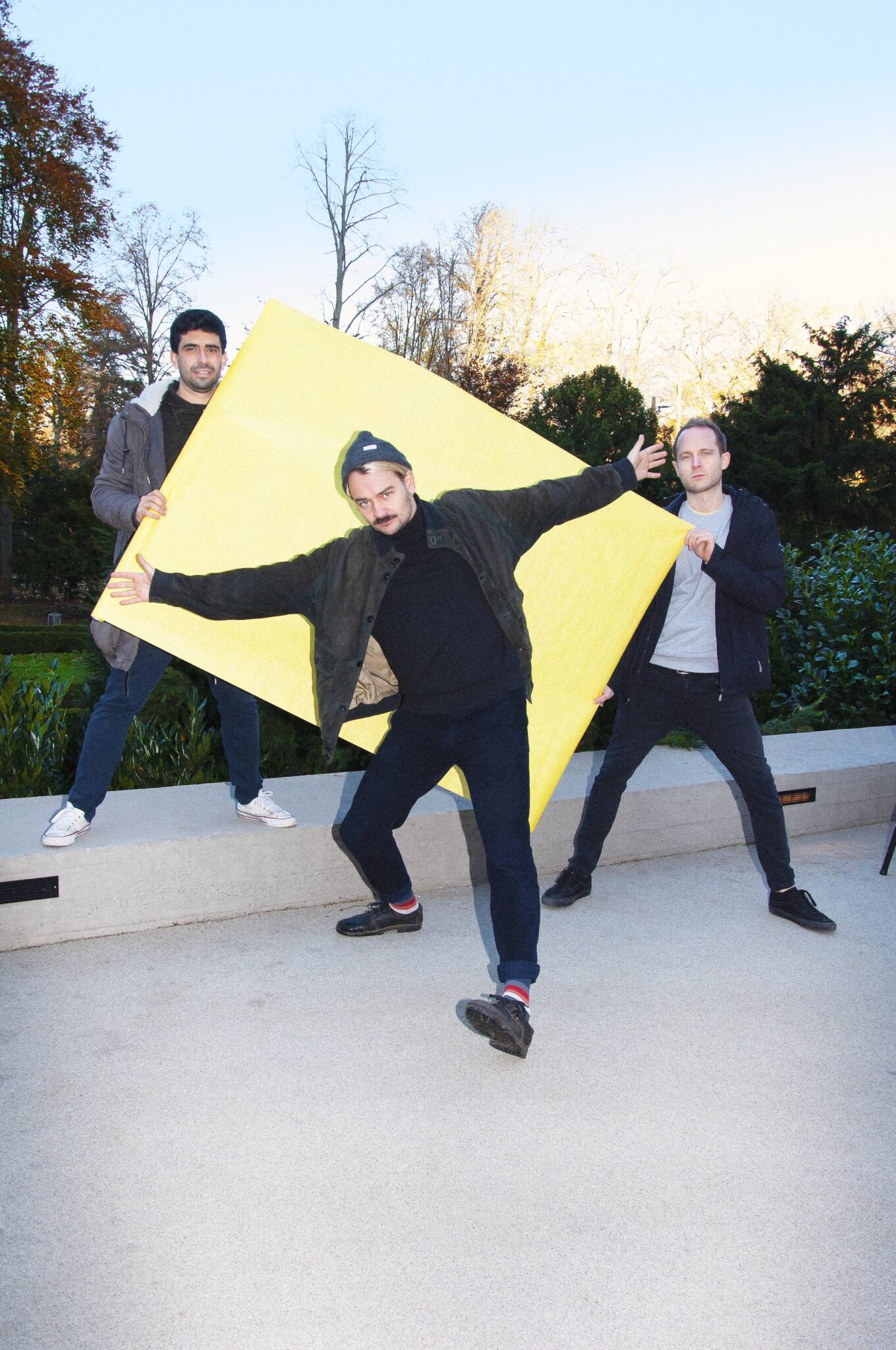 das Jazztrio Blind Spot posiert im Park mit einem großen, gelben karton.