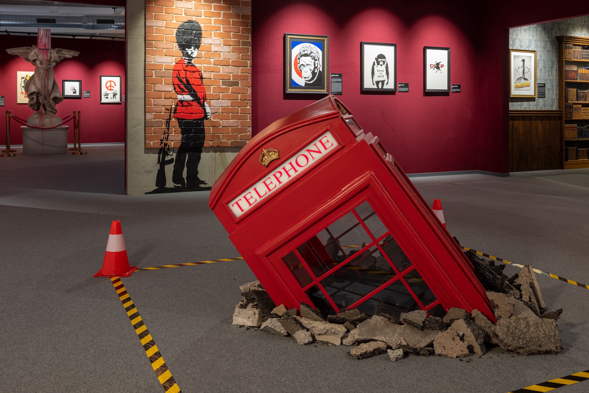 The Mystery of Banksy: Zu sehen sind teile der Ausstelung, z.B. im Vordergrund: eine halb in den Boden gerammte, rote, englische Telefonzelle.