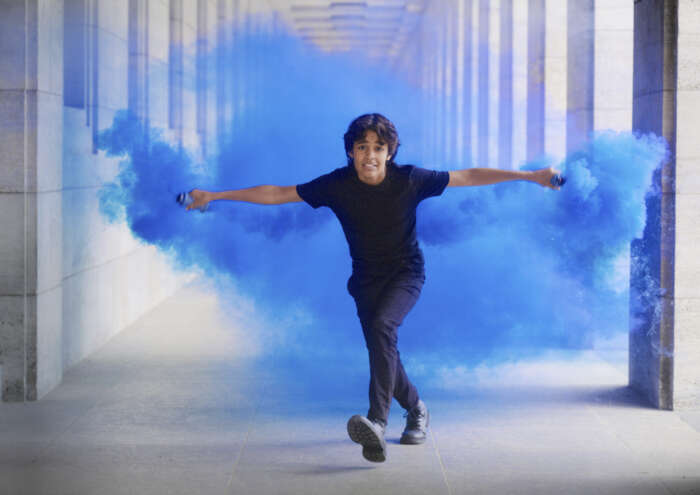 Zu sehen ist Hauptcharakter Tanji, ein Junge aus Indien, der seine Hände mit blauen, rauchenden Bengalos ausstreckt.