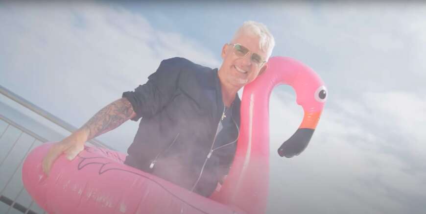 Heinz Strunk mit Sonnenbrille auf und einem aufblasbaren Flamingo.