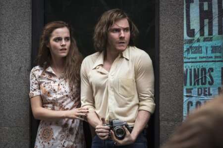 Still aus „Colonia Dignidad“: Emma Watson und Daniel Brühl stehen nebeneinander in einem Hauseingang, sie wirken panisch. Watson hält sich an Brühls Arm fest, der eine Kamera in den Händen hält.