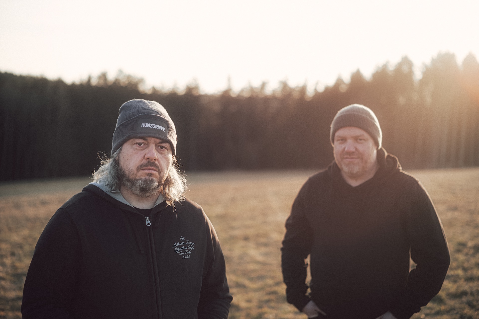 Die beiden Musiker von Hunzgrippe sind vor einem Waldstück zu sehen.