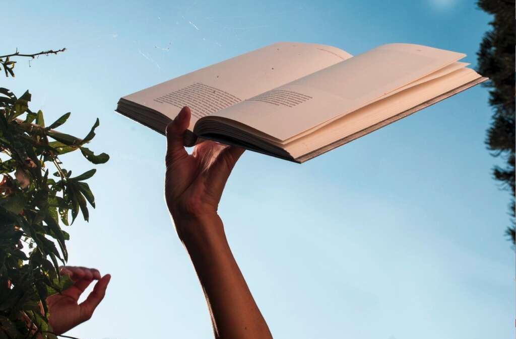 Ein Hand hält gegen den blauen Himmel ein geöffnetes Buch hoch.