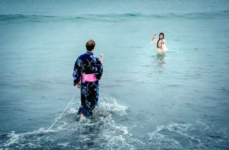 Still aus „Kirschblüten und Dämonen“: Ein Mann geht über das Wasser auf eine Frau zu, die bis zu den Hüften im Wasser steht.