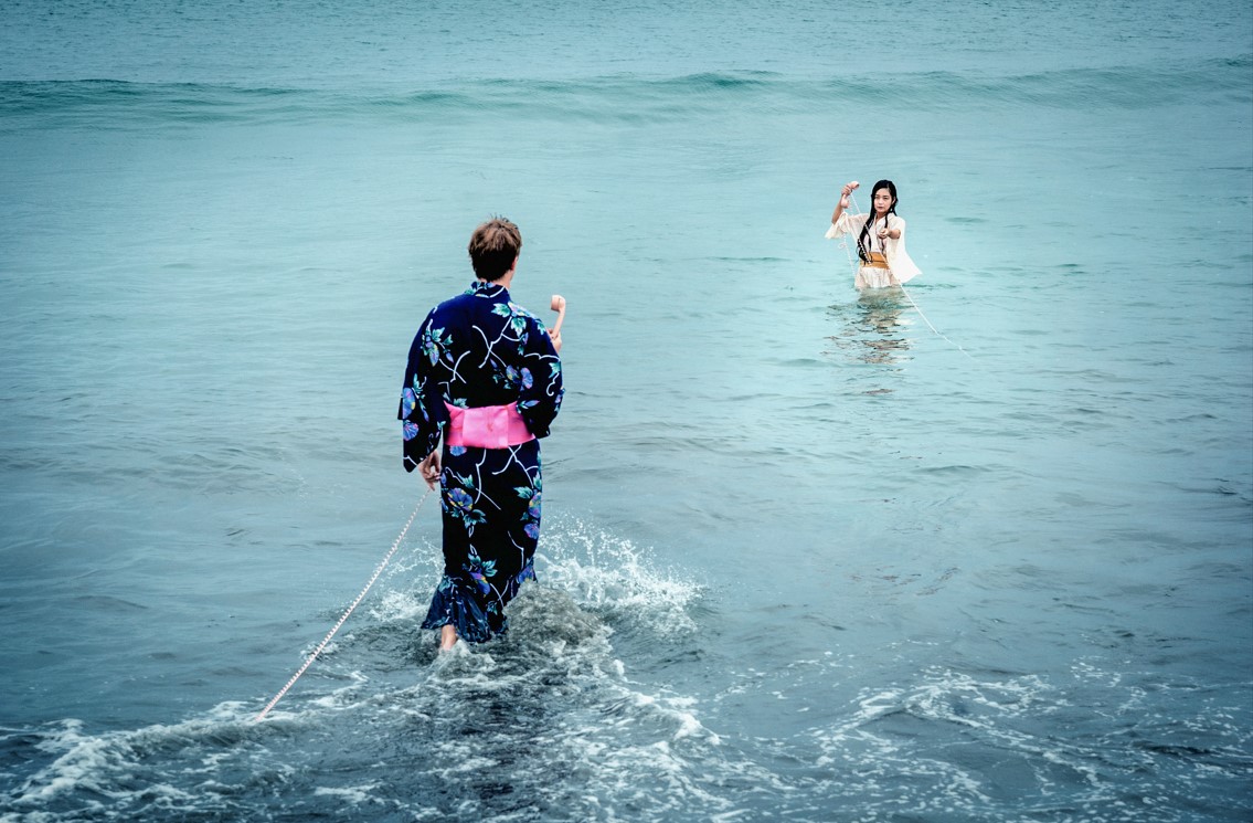 Still aus „Kirschblüten und Dämonen“: Ein Mann geht über das Wasser auf eine Frau zu, die bis zu den Hüften im Wasser steht.