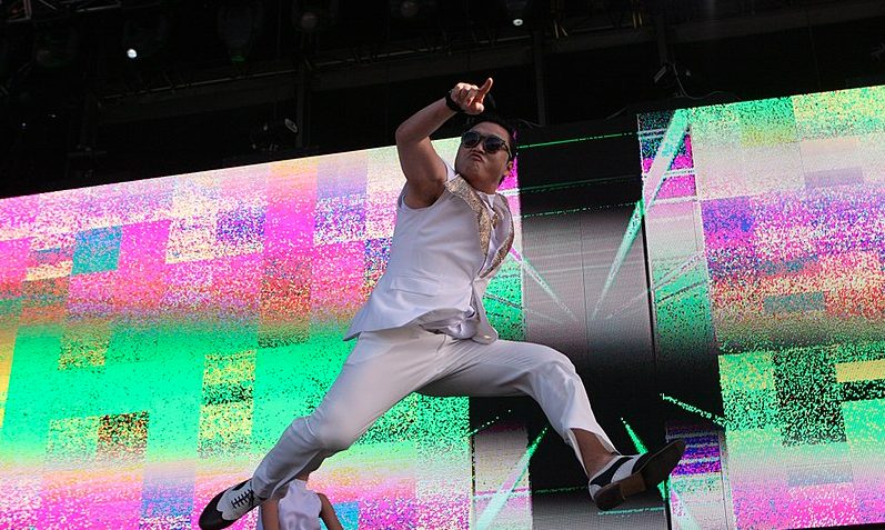 Rapper Psy auf der Bühne, er trägt einen weißen Anzug ohne Ärmel und eine Sonnenbrille.