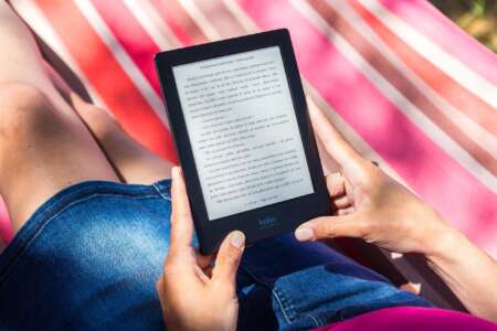 Bücher, Hitze, Wochenende: Zu sehen ist ein Frau im Jeansrock auf einer gestreiften Decke, mit einem E-Reader in der Hand.