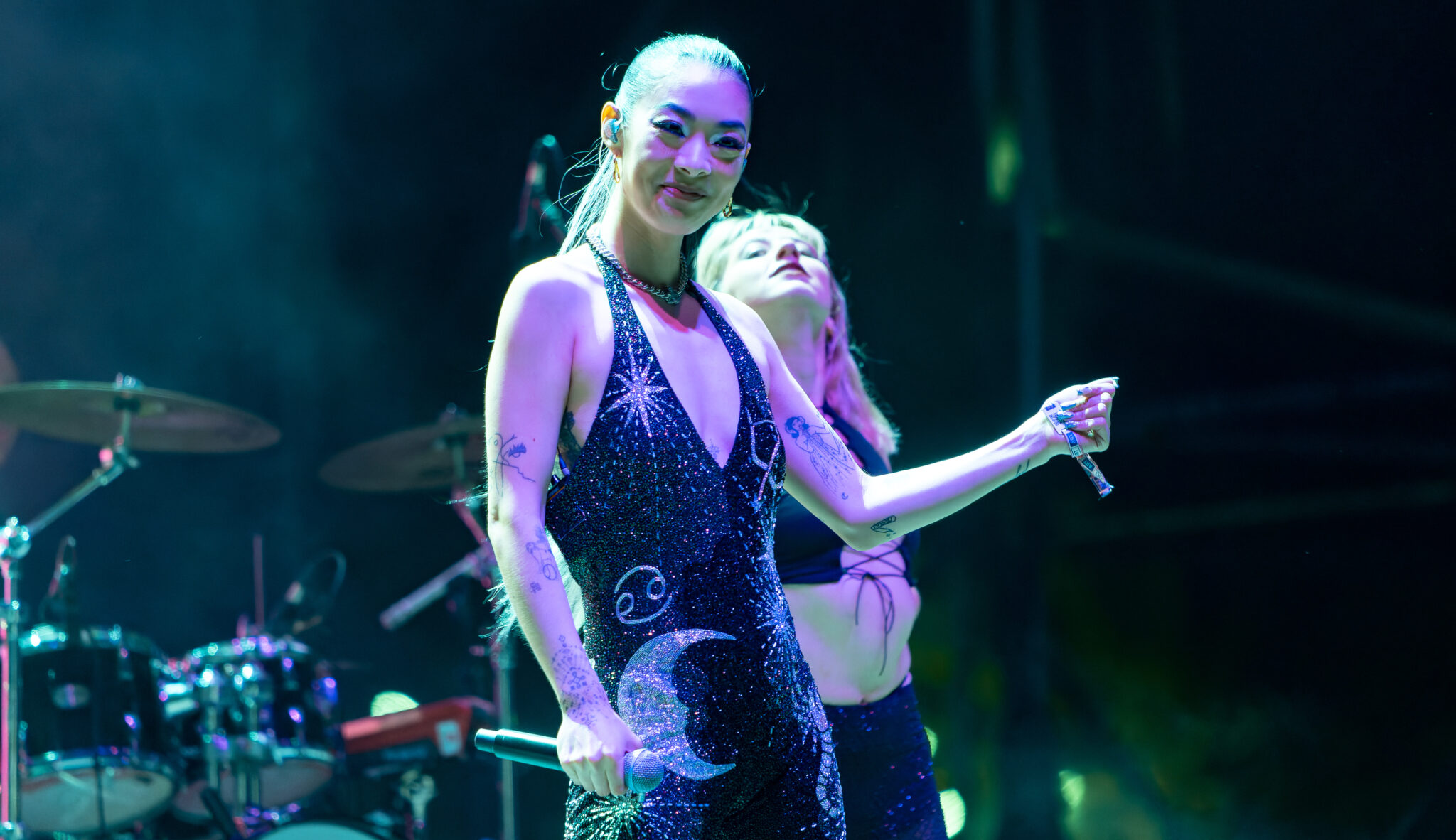Man sieht Rina Sawayama in einem schwarzen Kleid mit silbern glitzernden Sternen und Mond auf einer Bühne.