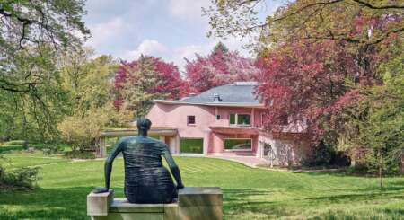 Die Skulptur einer Frau schaut auf ein rosafarbenes Haus