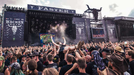 Zu sehen ist eine Bühne auf dem Wacken Festival, davor tobt eine wilde Festival-Crowd.