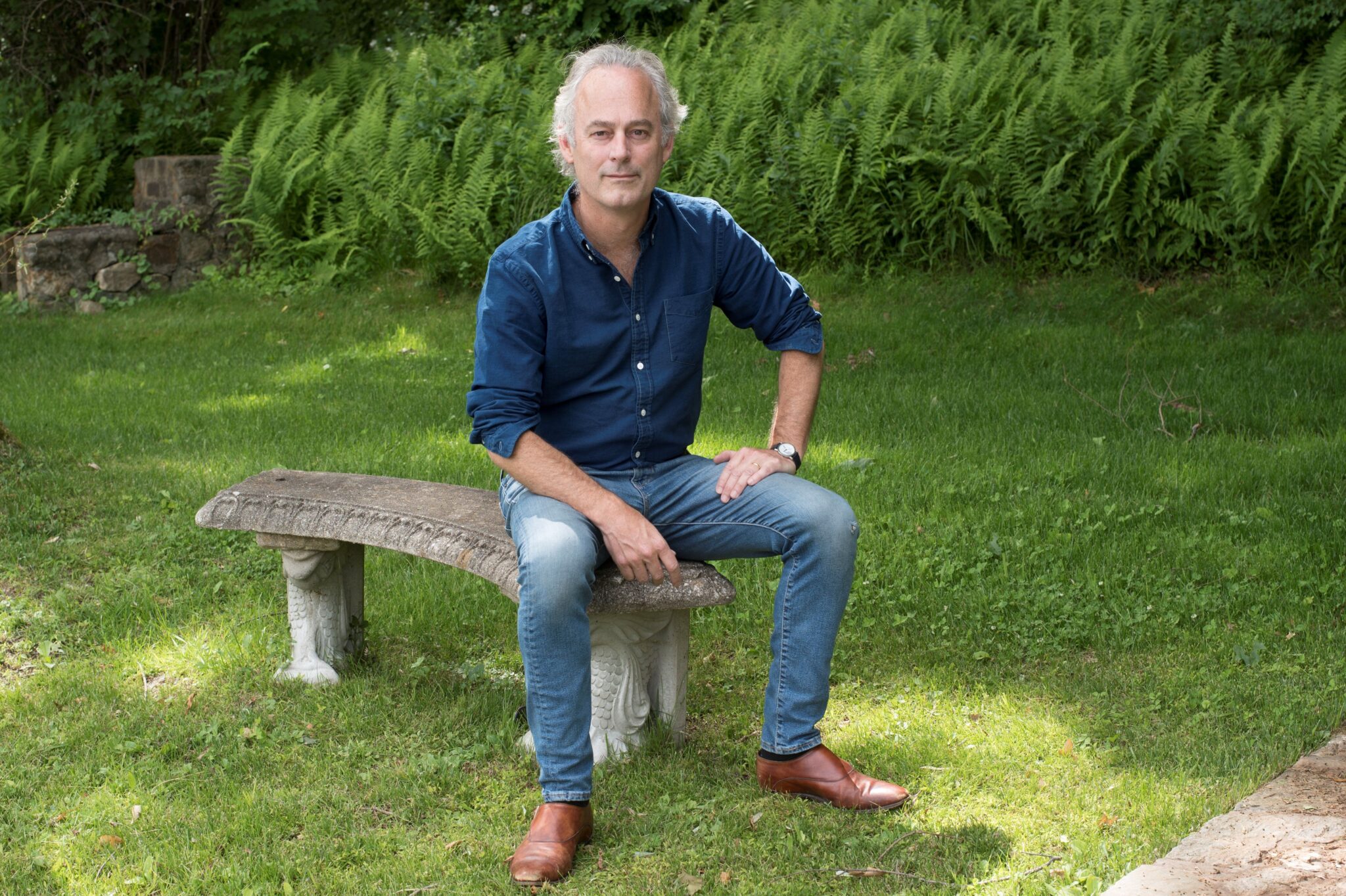 Amor Towles sitzt auf einer Bank im Park.