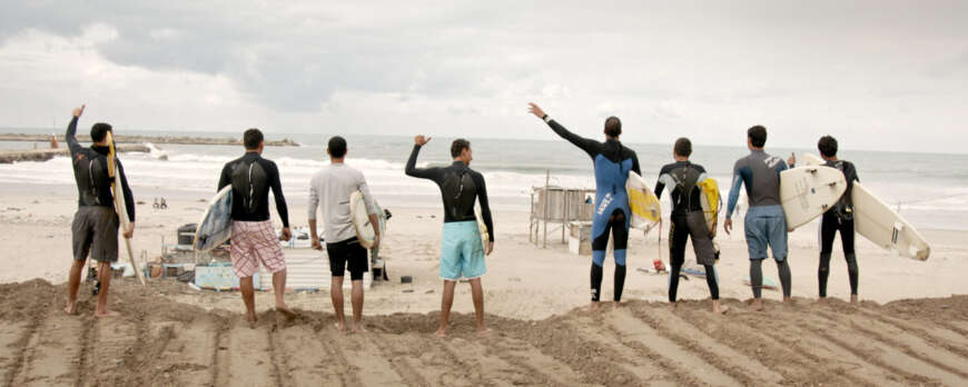 TV-Tipp „Gaza Surf Club“: Man sieht einen leeren Strand, im Vordergrund stehen junge Menschen mit Surfbrett zum Meer hingewand (von hinten zu sehen).