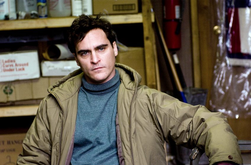 Still aus „Two Lovers“: Joaquin Phoenix sitzt unzufrieden da, er trägt eine Jacke, ist aber drinnen.