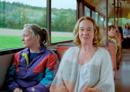 Caro (Silke Bodenbender, li.) und Frau Rumi (Klara Höfels) sitzen nebeneinander im Bus. Caro blickt aus dem Fenster, Frau Rumi lächelt.