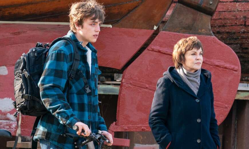 Still aus „Der Usedom-Krimi: Schneewittchen“: Der Teenager Theo steht auf einem Roller, neben ihm geht Karin Lossow. Im Hintergrund ein großes Schiffsruder..