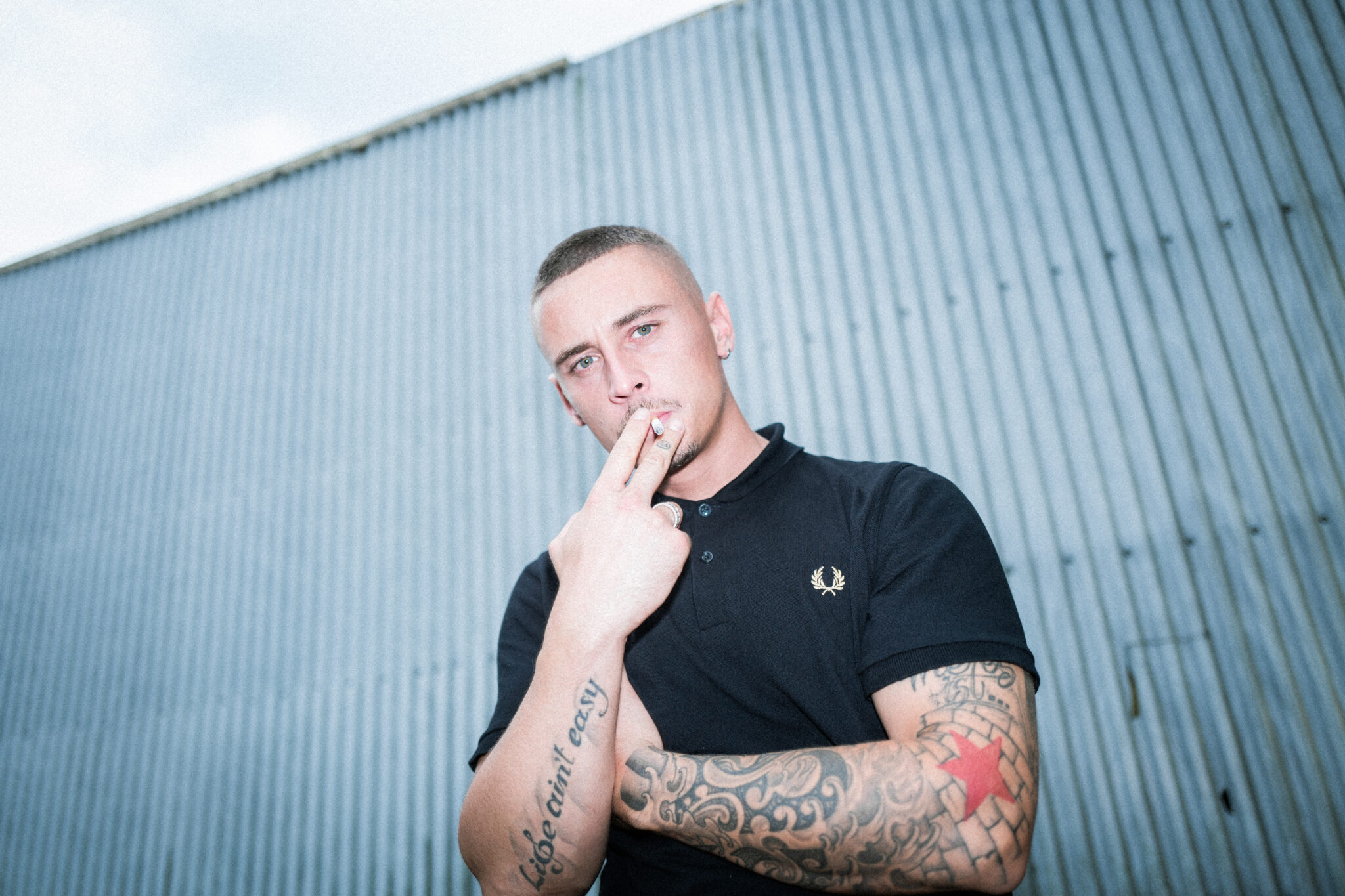 Disarstar steht vor einer Wand und raucht eine Zigarette.