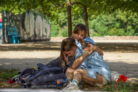 Die Schwestern Jaroslava (Maria Shtofa) und Nika (Oleksandra Barstok) sitzen in einem Berliner Park auf dem Boden und umarmen sich.