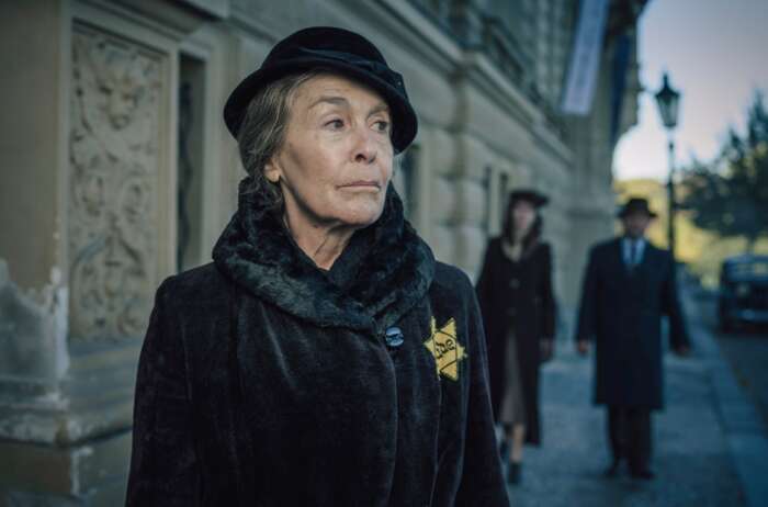 Still aus „Martha Liebermann – Ein gestohlenes Leben“: Martha Liebermann, eine alte Dame, auf der Straße. Sie trägt einen Hut und einen schwarzen Mantel, an dem ein Judenstern befestigt ist.