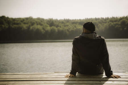 Ronny Mollenhauer sitzt auf Steg am See, von hinten fotografiert