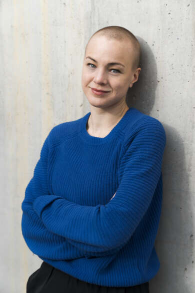 Portraitfoto Maria Muhar vor heller Wand, trägt blauen Pulli