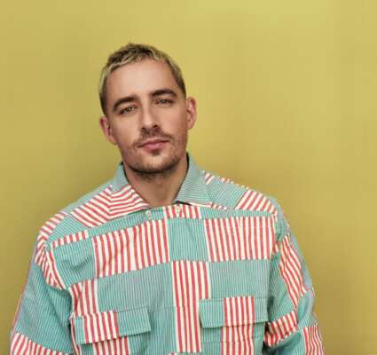 Dermot Kennedy steht in einem grün-rosafarbenem Hend vor einer gelben Wand.