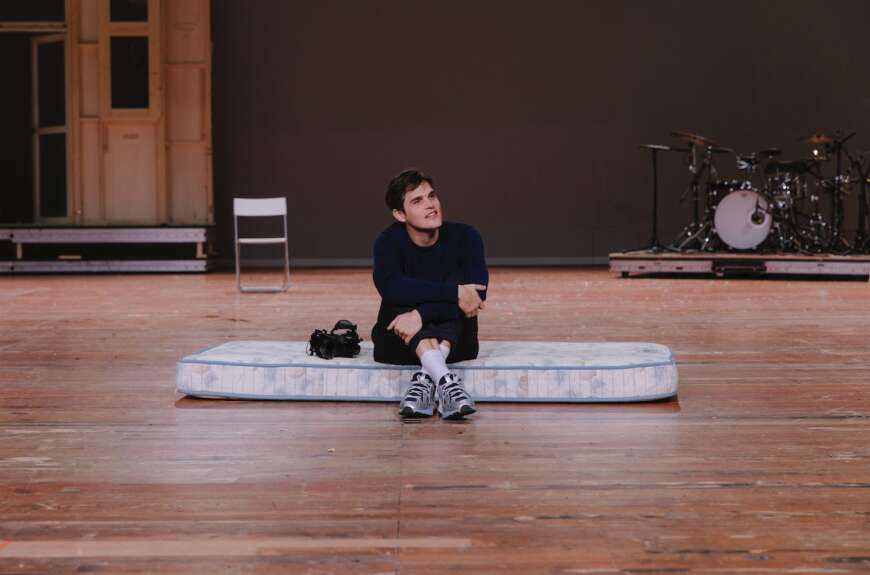 Ein Mann sitzt auf einer Matratze auf einer Bühne