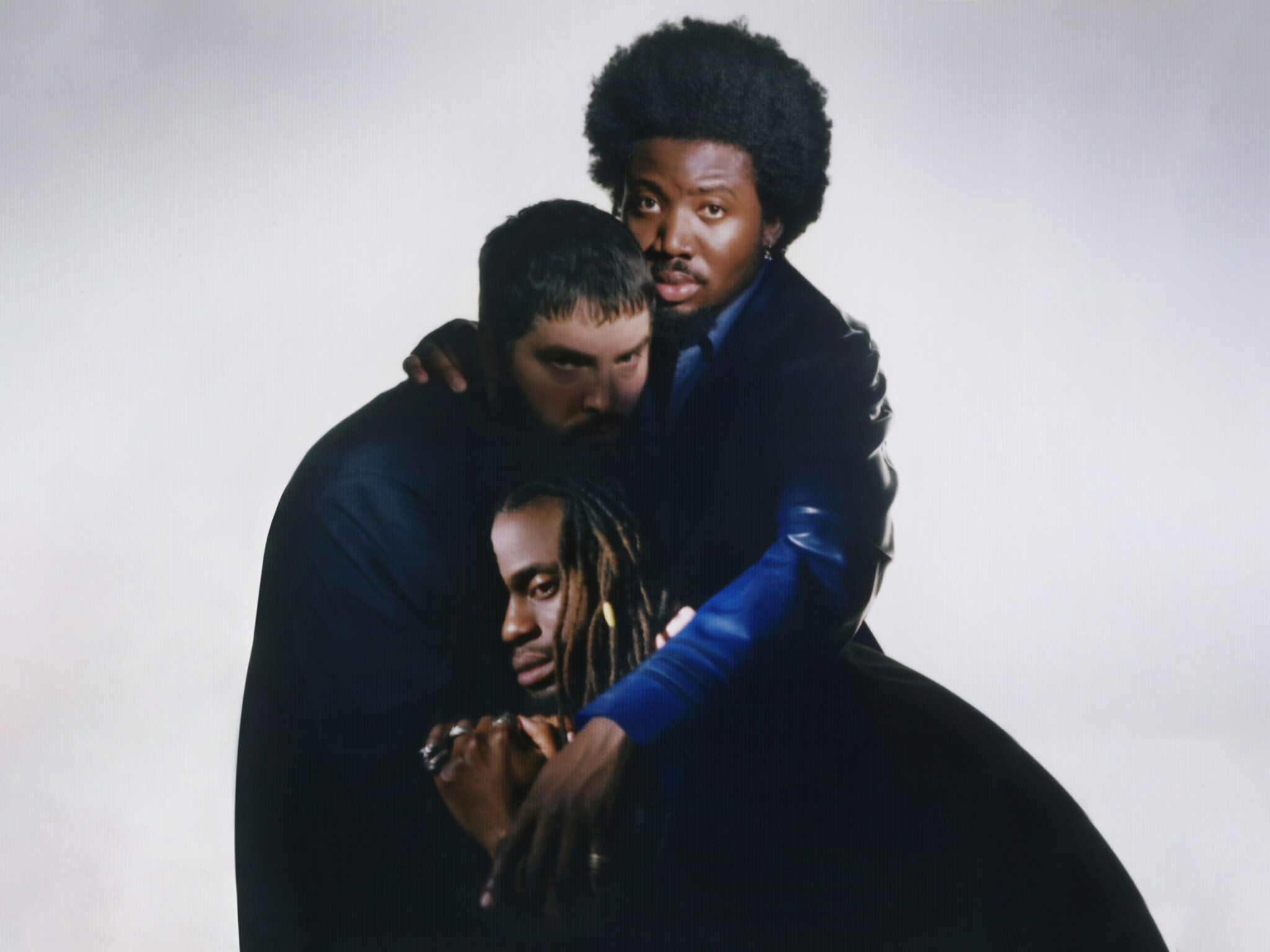 Kayus, G und Alloysious von den Young Fathers übereinander vor weißem Hintergrund.